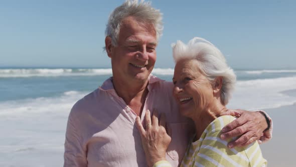 Happy senior caucasian couple with arms around each other embracing each other on the beach