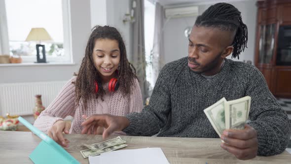 Front View Portrait of African American Rich Man Counting Dollars Sharing Money with Teen Girl