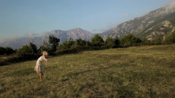 Aerial view of dancing blonde woman on the grass against the background of mountains