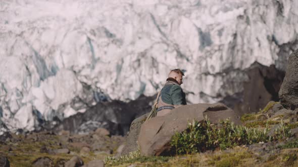 Traveller Carrying Guitar Case On Rocky Hill Next To Glacier