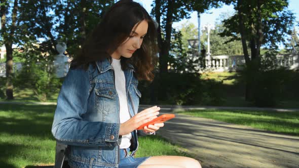 A Beautiful Girl is Sitting on a Park Bench on a Sunny Summer Day and Chatting with Friends on