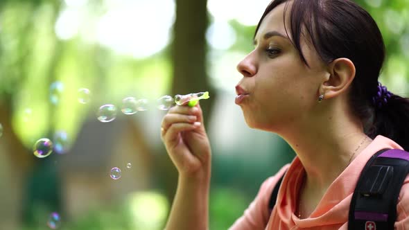 Young Woman Blowing Bubbles on Nature. Happy Young Brunette Woman Strolls in the Park and Makes Soap