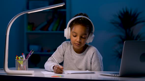 A Girl in Headphones Takes Notes While Listening to an Audio Lesson Looks at the Laptop Nods Her