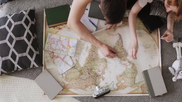 Young Couple Is Planning Traveling Route Pointing Places for Visit on a Map Using Red Flag Pins