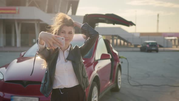 Caucasian Woman Takes a Selfie on a Smartphone in Front of a Luxurious Red Car