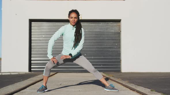 African american woman in sportswear stretching in street before exercising