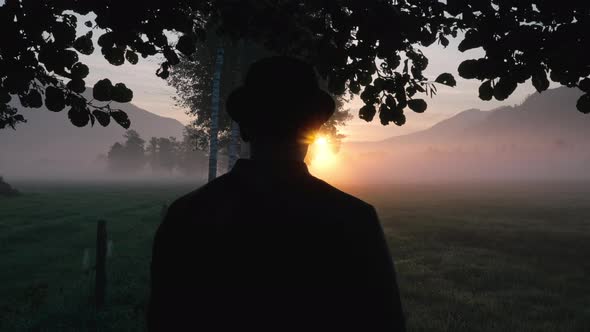 Man In Silhouette In Misty Meadow Watching Sunrise