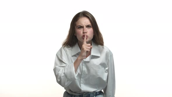 Attractive Young Brunette in White Collar Shirt Telling to Shut Up Showing Hush Sign and Frowning