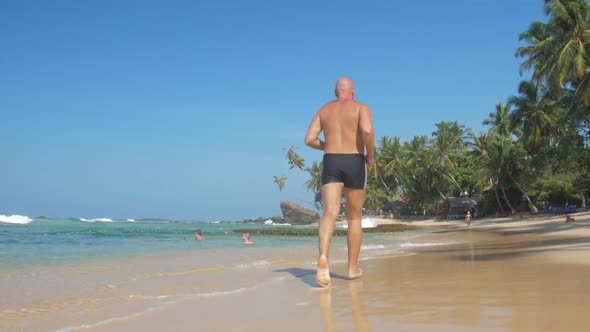 Bald Man Does Morning Jogging Against Swimming Tourists