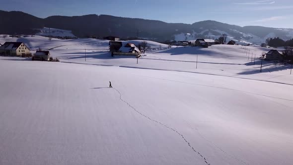 Young man walks in a huge snowy field and stops and looks around in Switzerland while winter.