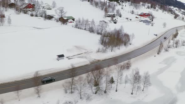 Cars Driving On The Road Passing By Houses And Fields Covered With Snow At Winter In Haugastol, Norw