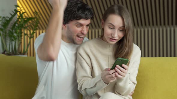 Married Couple Looking at Smartphone Screen Celebrating Online Lottery Win Notification