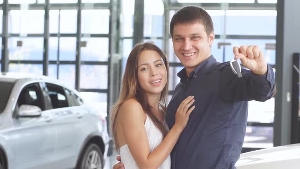 Handsome Caucasian Man Holding Car Keys in Hand Posing with His Gorgeous Girlfriend Near New Luxury