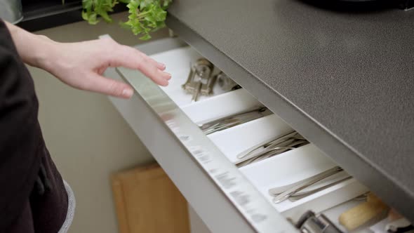 Girl or Woman in Black Tshirt and Short Shorts Walks Over to Cutlery Drawer and Picks Up Two Shiny