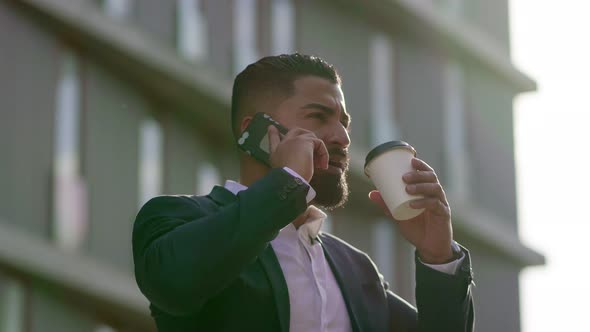 Man Drinking From Paper Cup and Talking By Smartphone