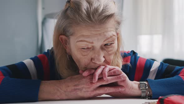 Desperate Old Woman Pensioner Looking at Small Amount of Coins on the Table