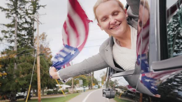 Happy Middle-aged Woman with an American Flag. Looks Out the Window of a Moving Car. Slow Motion