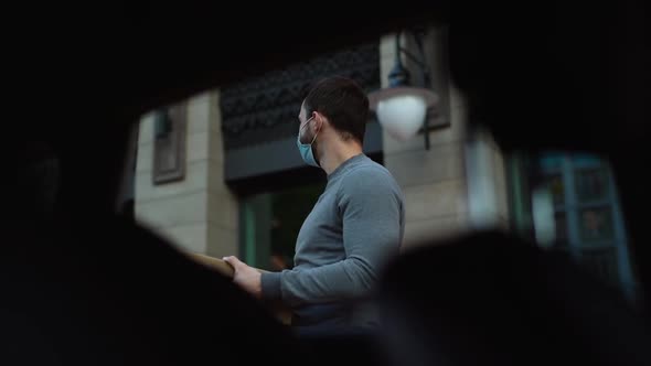 Low-angle shot of delivery man in mask holding cardboard boxes and rotates head in search customer.