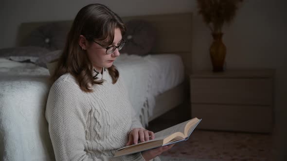 Young woman reading book in cozy room, turning page