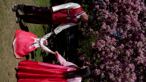 Korean Family in National Costumes in Nature Stands Next to a Cherry Blossoming Tree