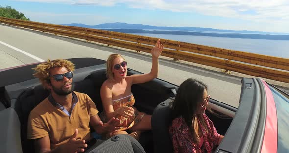 Young happy people on summer holiday having fun driving in red convertible