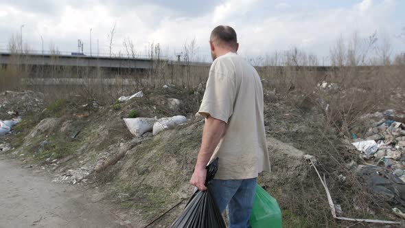 Man Walking along Garbage Dump with Trash Bins