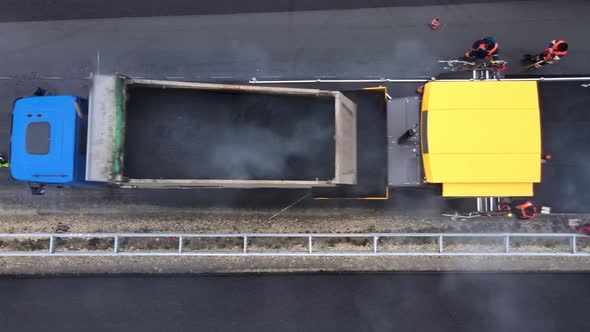 A view from above of a truck loading hot asphalt into a paver. Road repair work