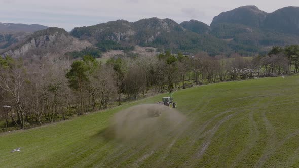 Drone view of tractor spraying fertilizer on field, seagulls in flight