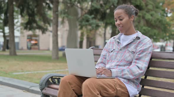 African Woman Celebrating Success on Laptop While Sitting Outdoor on Bench