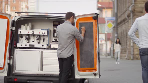 Barista Writing Menu on Chalkboard of Coffee Van