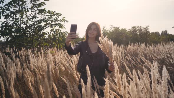 Attractive Fun Stylish Redhead Woman in the Field at Sunset Making a Selfie with a Bouquet of