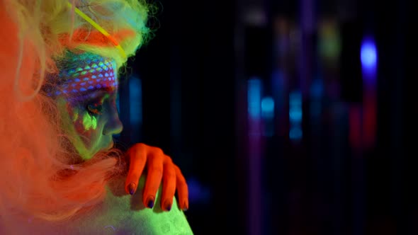 Eccentric Woman with Fluorescent Paint on Face and Body in Nightclub Side Portrait in Darkness