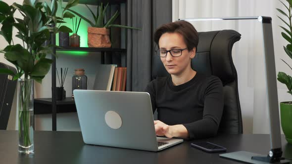 Businesswoman in glasses is opening laptop and starting to type on keyboard. Woman works on computer