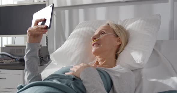 Aged Female Patient with Breathing Tube Having Video Call on Tablet Pc Lying in Hospital Bed