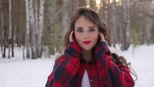 Young Woman with Wavy Hair Standing and Touching Face in Winter Forest