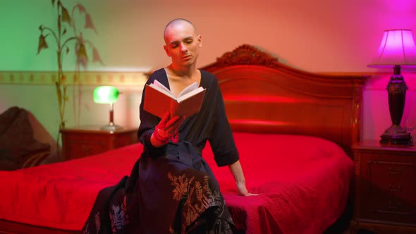 Young Male Queer Reading Book in Red Bedroom at Home