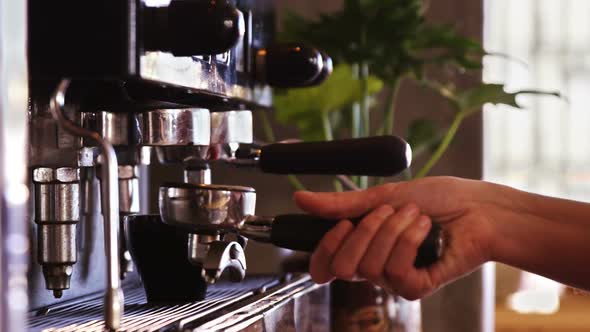 Waitress using a tamper to press ground coffee into a portafilter