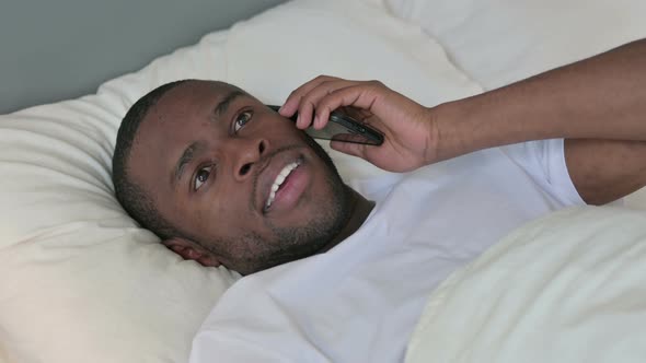 African Man Talking on Smartphone Laying in Bed 