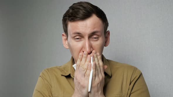 Sick Man Sneezes Hard Wiping with White Napkin Standing on Grey Background