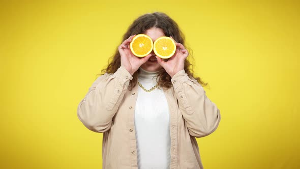 Cheerful Smiling Plussize Woman Holding Half Oranges Over Eyes Smiling Looking at Camera