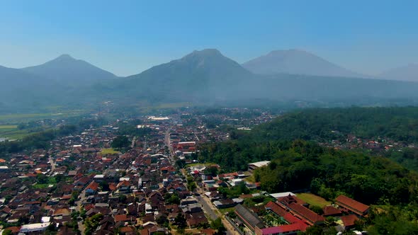Grabag village in valley below majestic Java volcanoes silhouettes aerial view