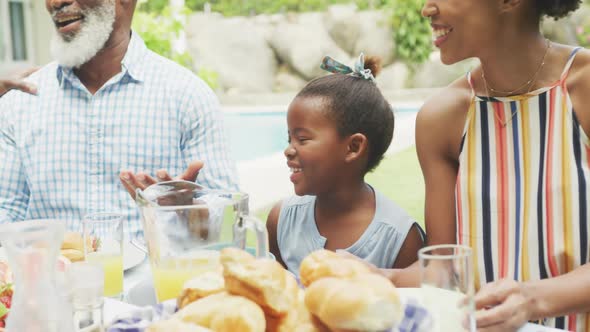 Happy african american family talking and having breakfast in garden