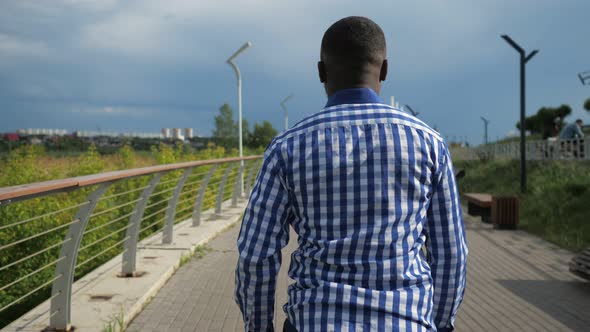 Young Afro American Man is Walking in City Park in Cloudy Summer Day