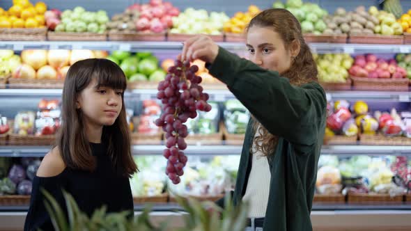 Two Cheerful Girls Choosing Bio Fruits  Grape in Supermarket Together