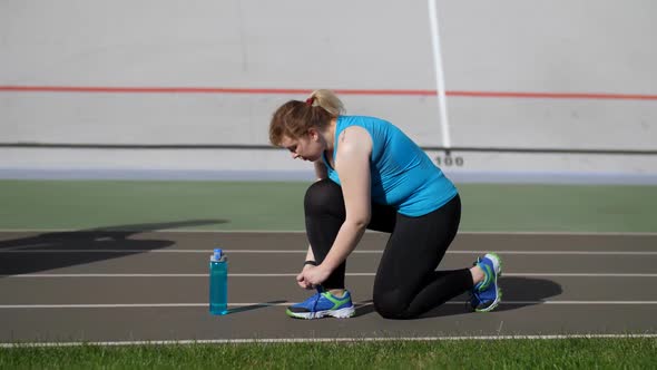 Active Fat Woman Runner Tying Shoelaces on Stadium