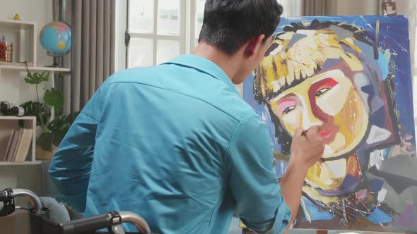 Asian Artist Man In Wheelchair Holding Paintbrush Painting A Girl's Face On The Canvas