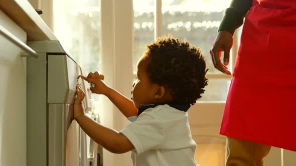 Side view cute little black son playing at washing machine in kitchen of comfortable home 4k