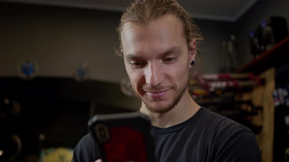 Young Man With Phone In His Hands Standing In Bicycle Workshop