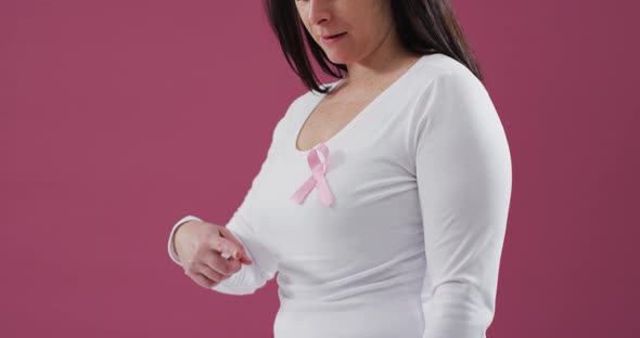 Mid section of a woman pointing to the pink ribbon on her chest against pink background