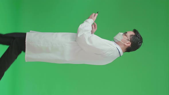 Asian Doctor With Stethoscope Wearing Mask, Using Mobile Phone While Walking On Green Screen